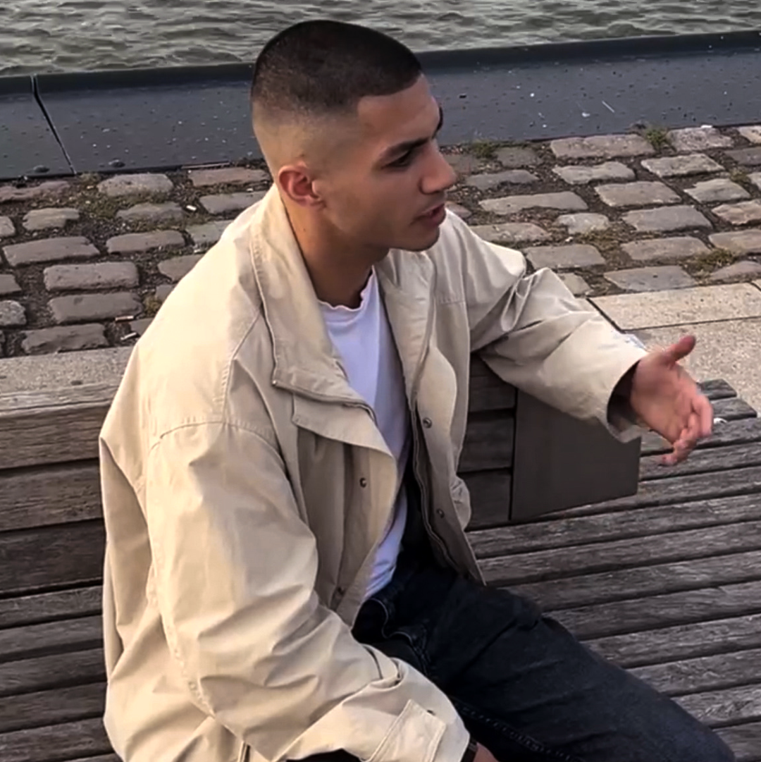Alvin sitting on a wooden bench by a waterfront and share his story for Origin.