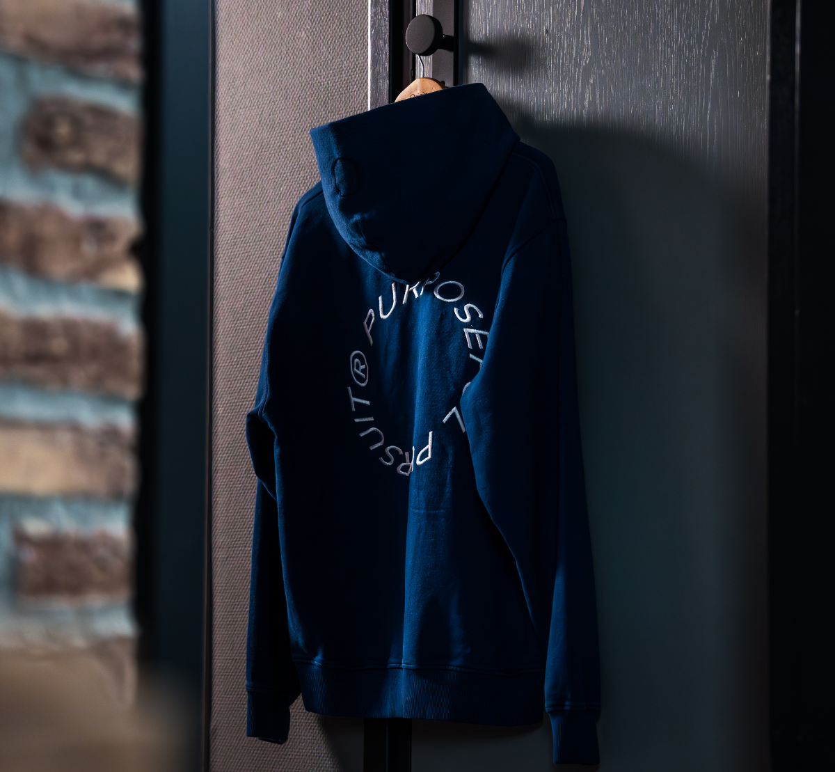 Indigo Blue Prelude Hoodie Origin. on a hook against a dark wall.
