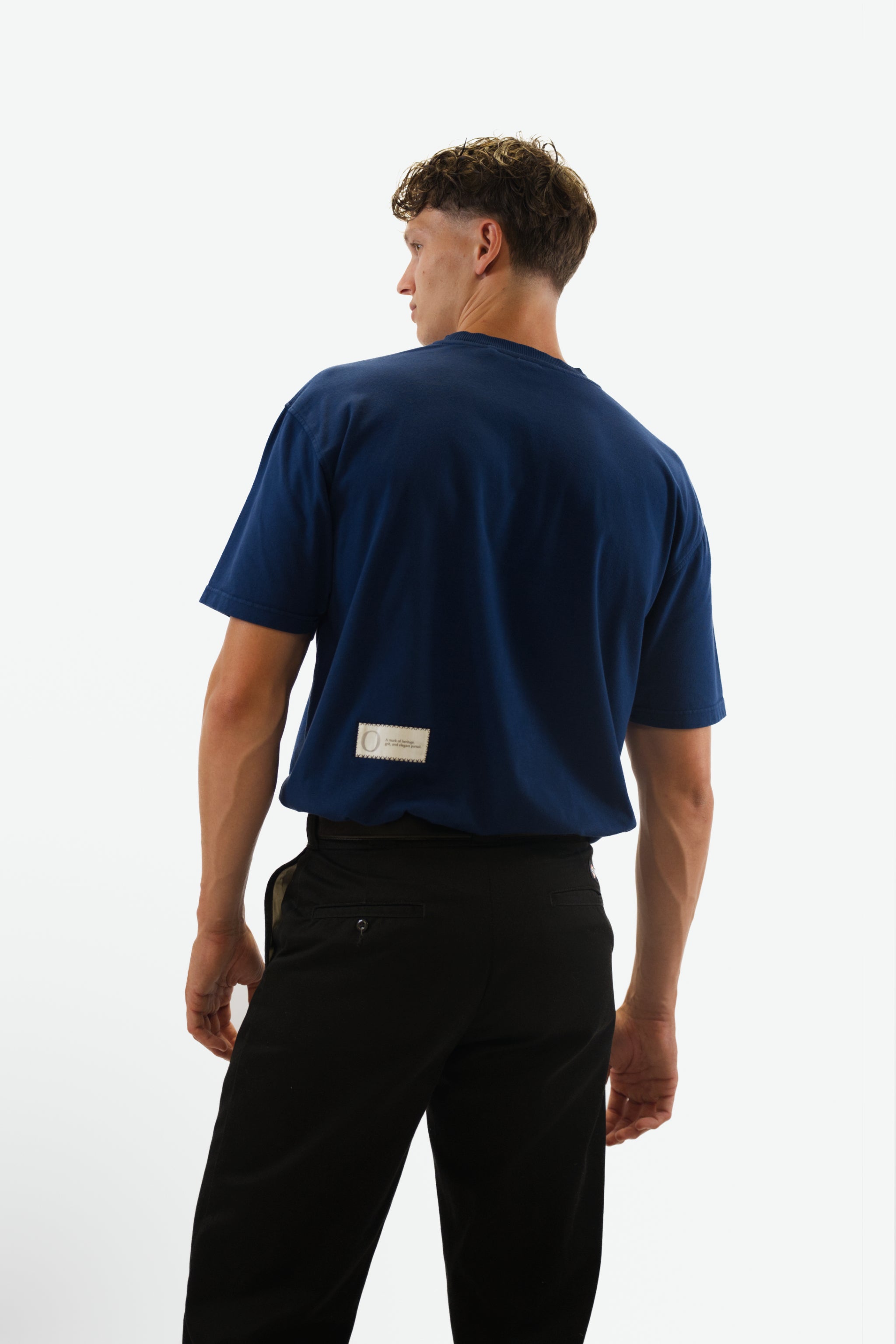 Back view tucked in of model wearing the Foundation Tee in indigo blue from Origin. made from organic cotton in a clean studio setting.