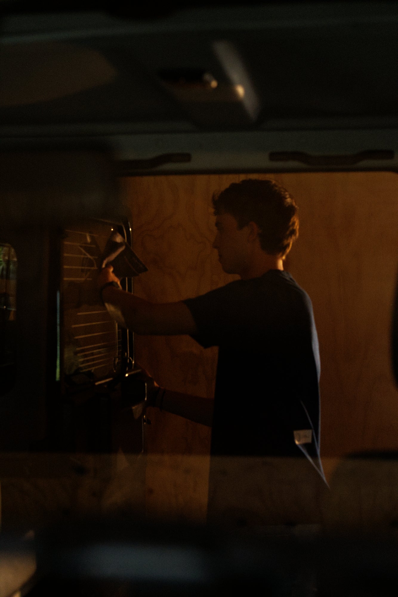 Model wearing the Foundation Tee in indigo blue from Origin. and is polishing a  Land Rover Defender  in a dimly lit room.