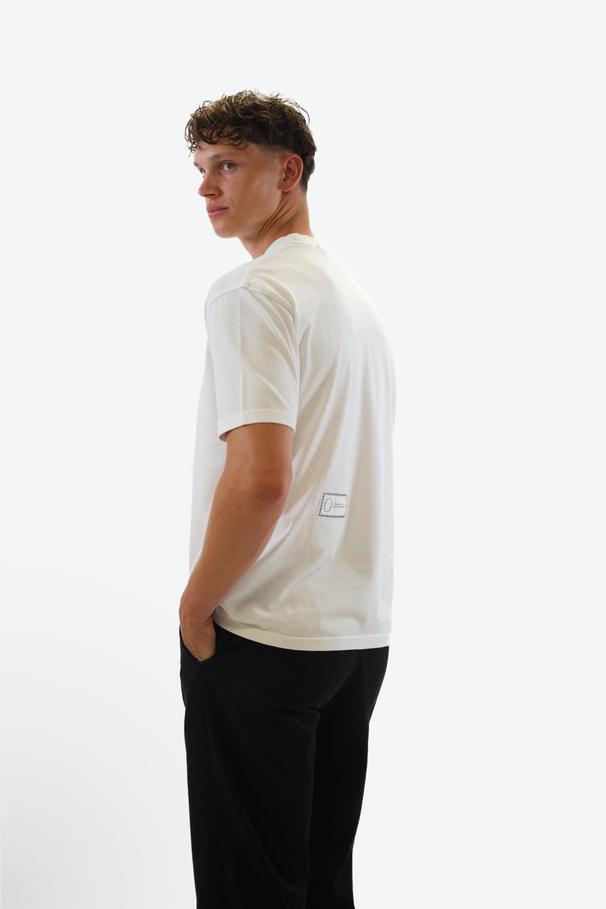 Side view of model wearing the Foundation Tee in white from Origin. made from organic cotton in a clean studio setting.