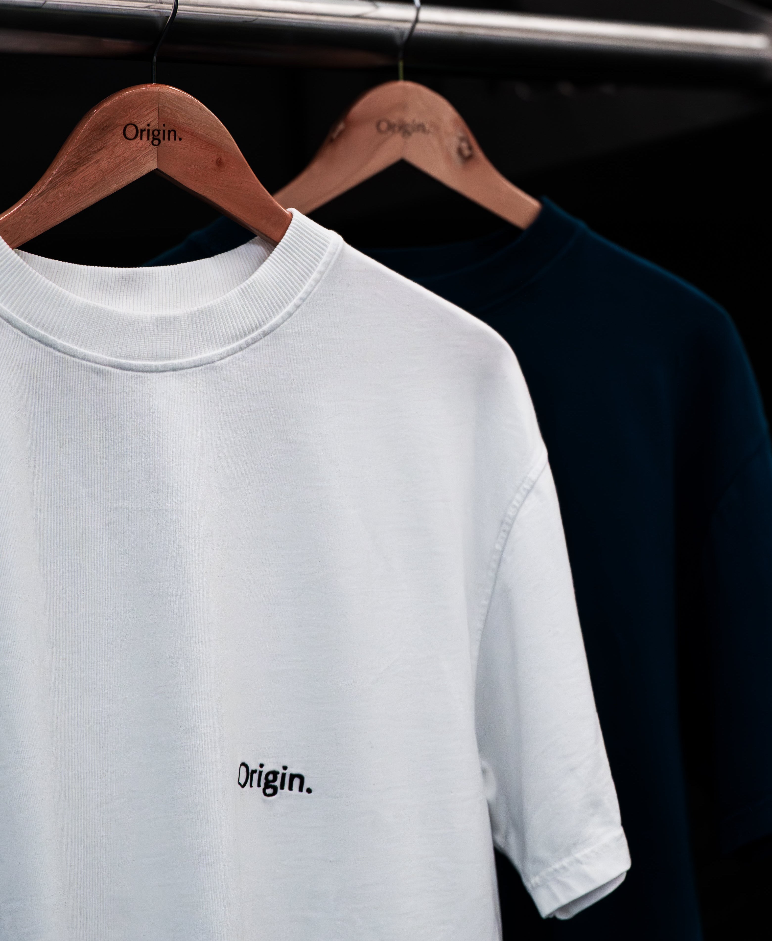 Foundation Tee White and Indigo Blue Origin. organic cotton t-shirts with front embroidery, hanging on wooden hangers.
