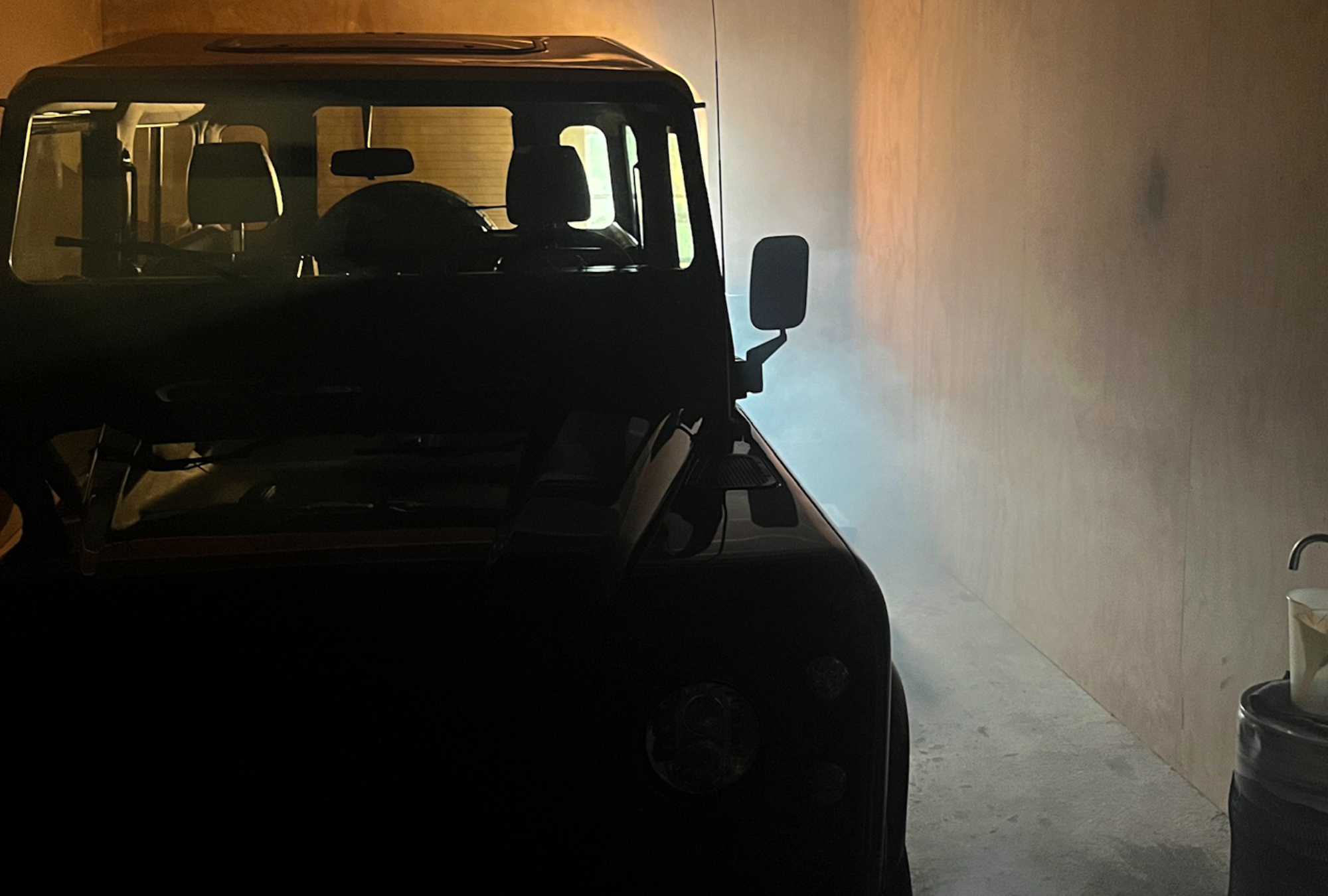 Front view of a Land Rover Defender from Origin. in a dark/dimly/foggy lit garage.