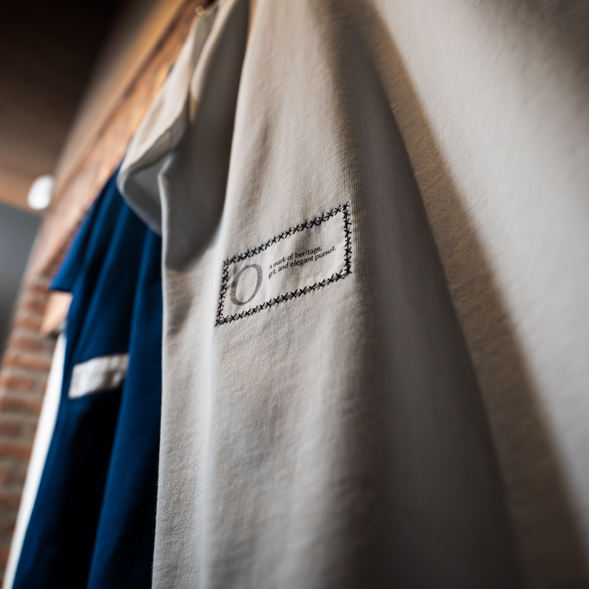 Foundation Tee White and Indigo Blue Origin. on a wooden rack against a brick wall.