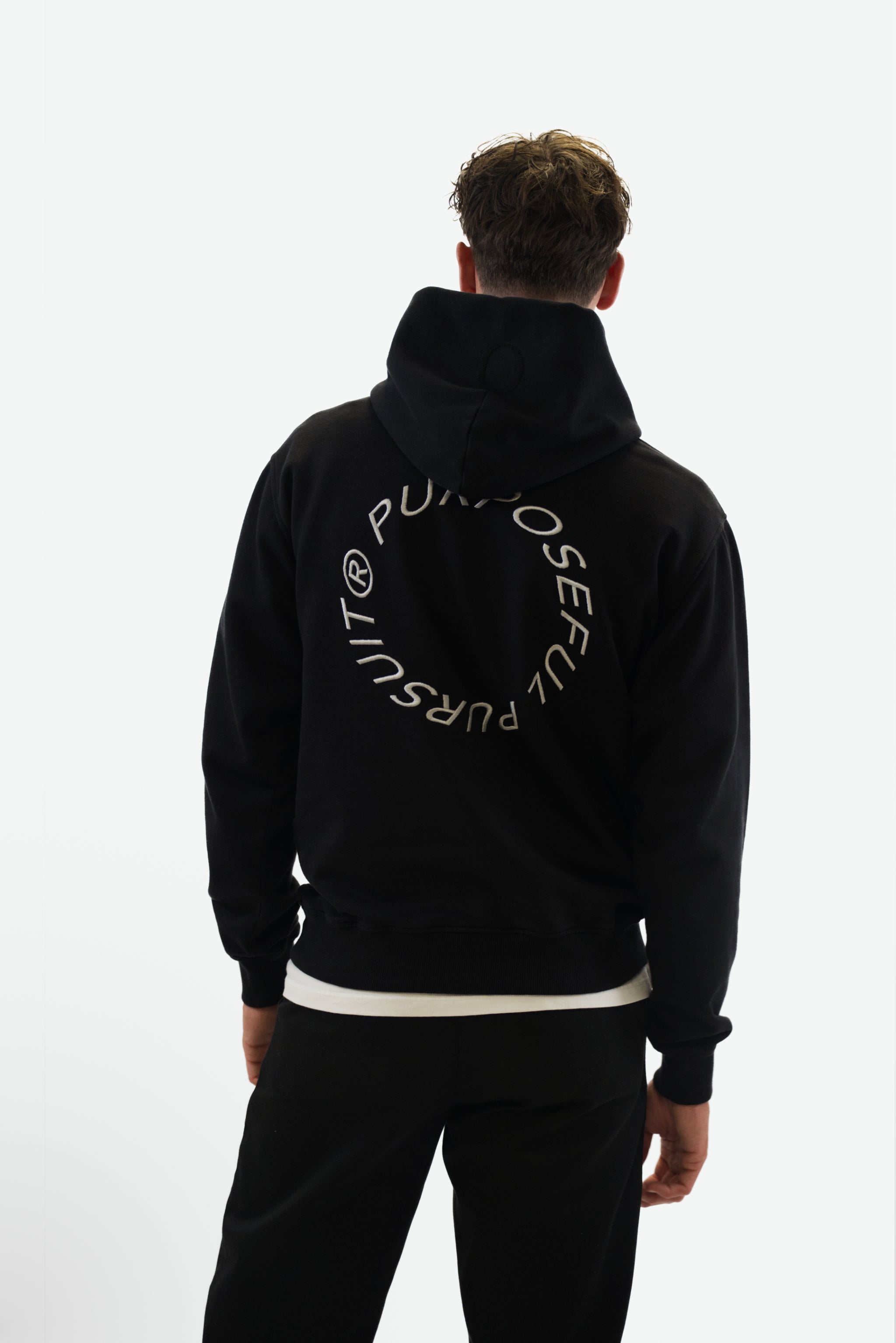 Back view of model wearing the Prelude Hoodie in black from Origin. made from organic cotton in a clean studio setting.