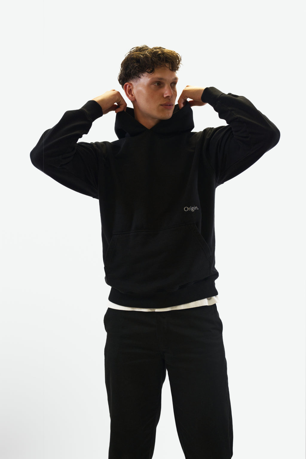 Front view grab the hood of model wearing the Prelude Hoodie in black from Origin. made from organic cotton in a clean studio setting.