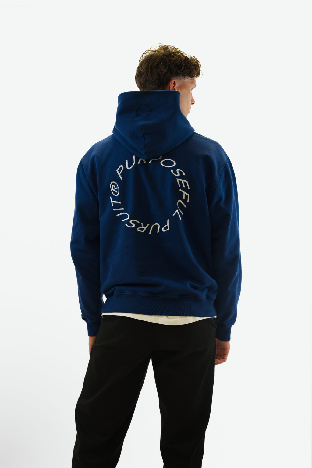 Back view of model wearing the Prelude Hoodie in indigo blue from Origin. made from organic cotton in a clean studio setting.