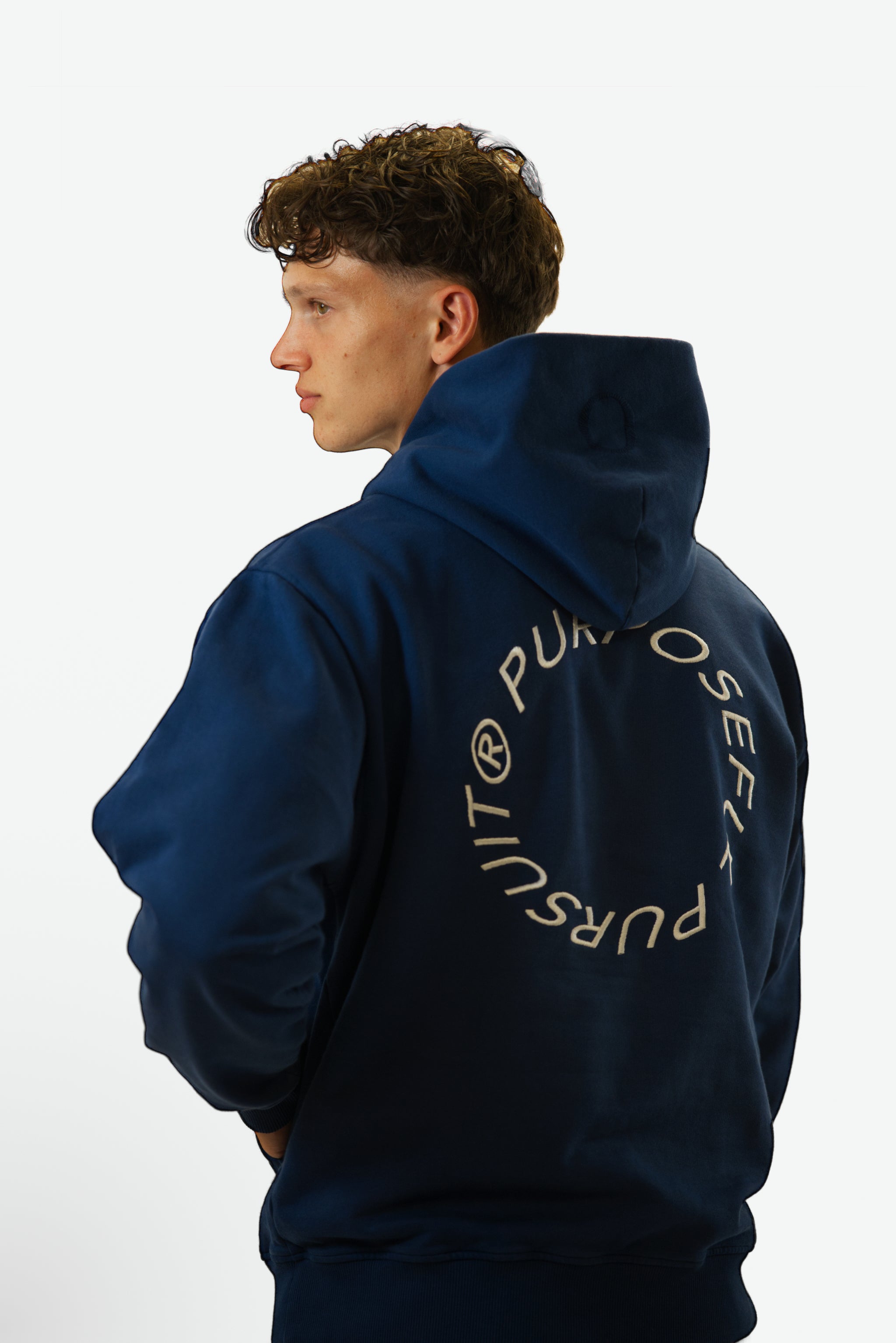 Back view close-up of model wearing the Prelude Hoodie in indigo blue from Origin. made from organic cotton in a clean studio setting.