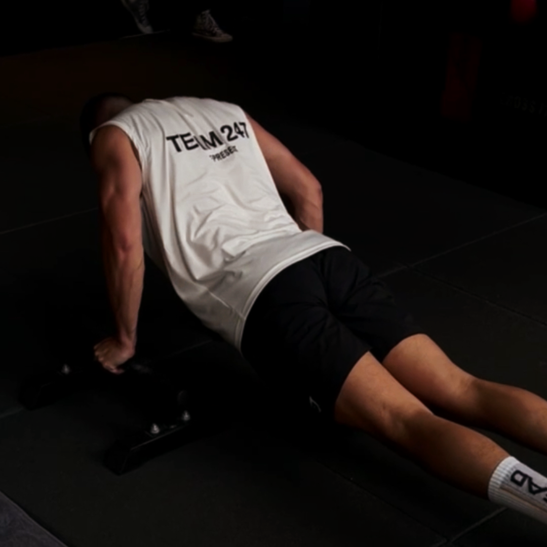 Alvin performing push-ups on a dark background wearing a white tank top.