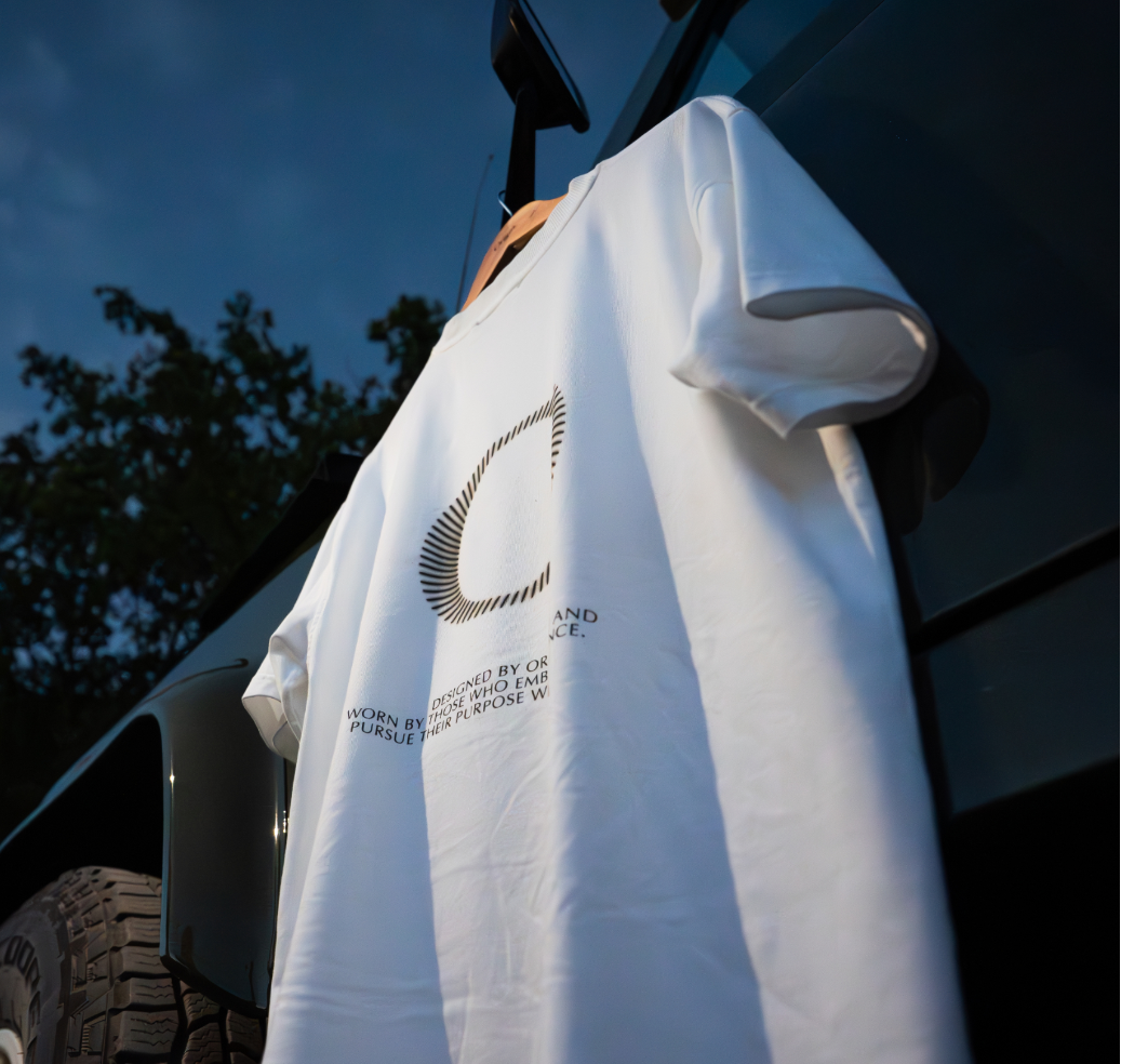 White Origin. Slash Tee hanging on a  Land Rover Defender door against a blue sky.