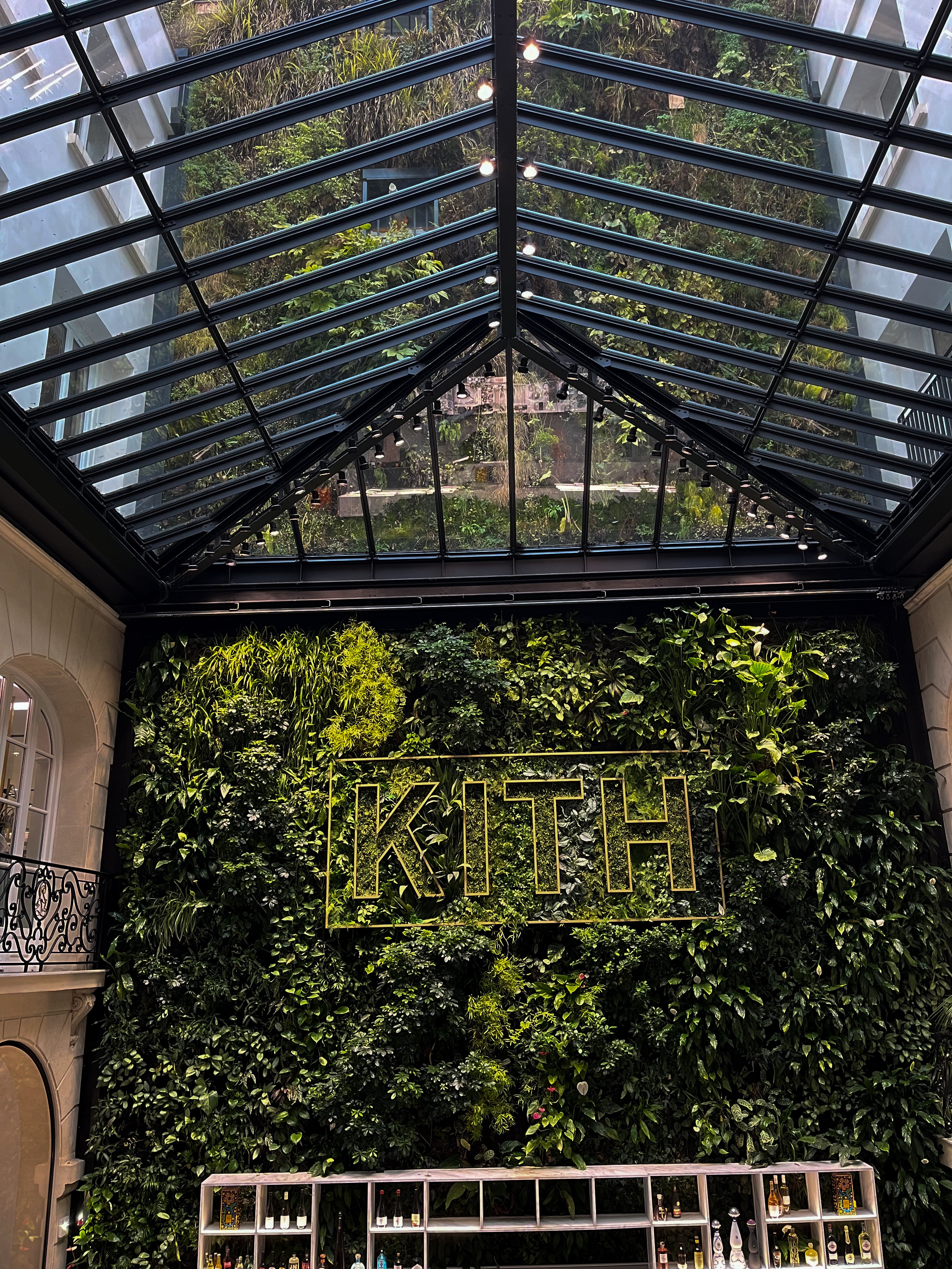 Indoor garden with a glass roof and logo in the centre and a bar below it. 