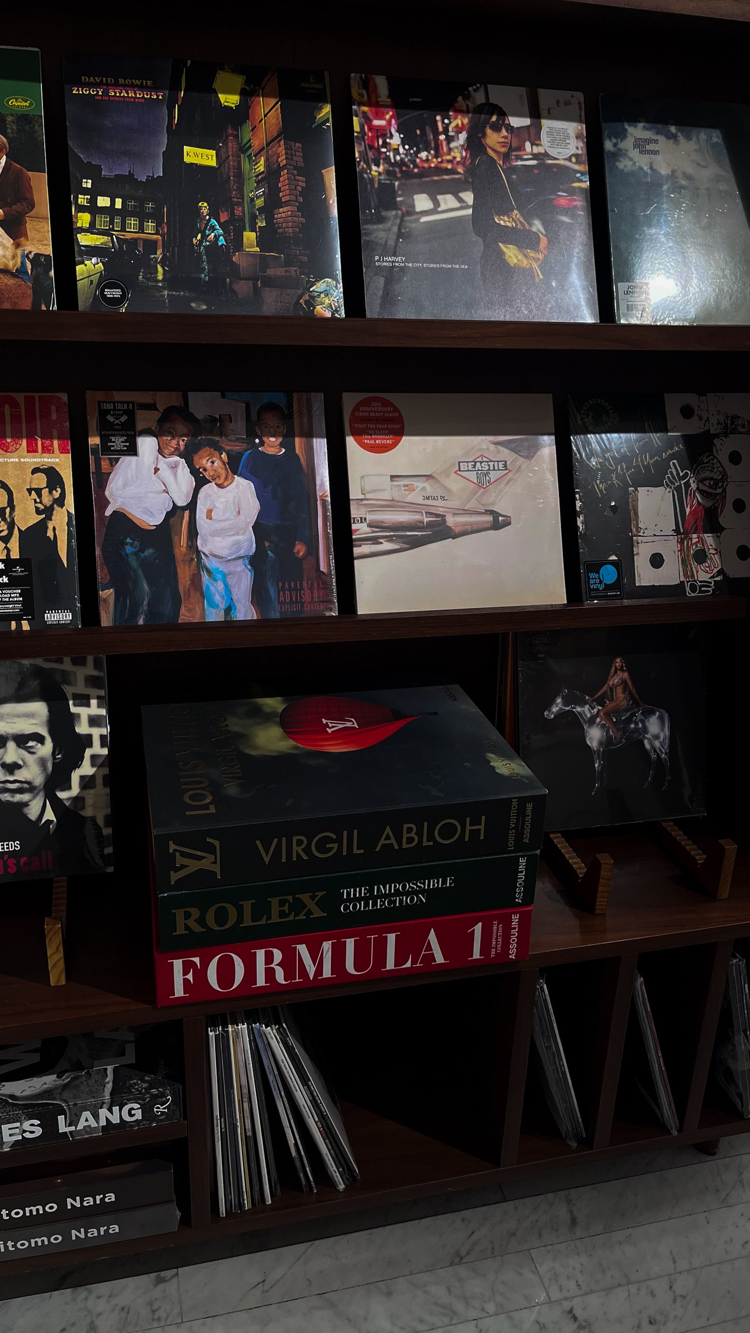 Collection of vinyl records and luxury books on a shelf with a dark brown colour.