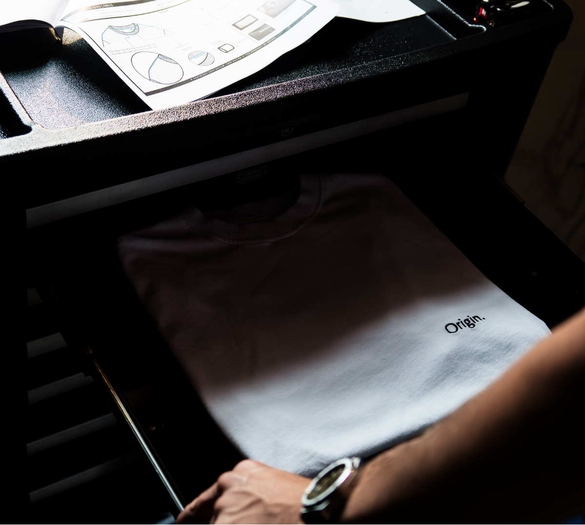 Model places The Slash Tee Origin. in white, nealty folded in an open drawer of a toolbox.