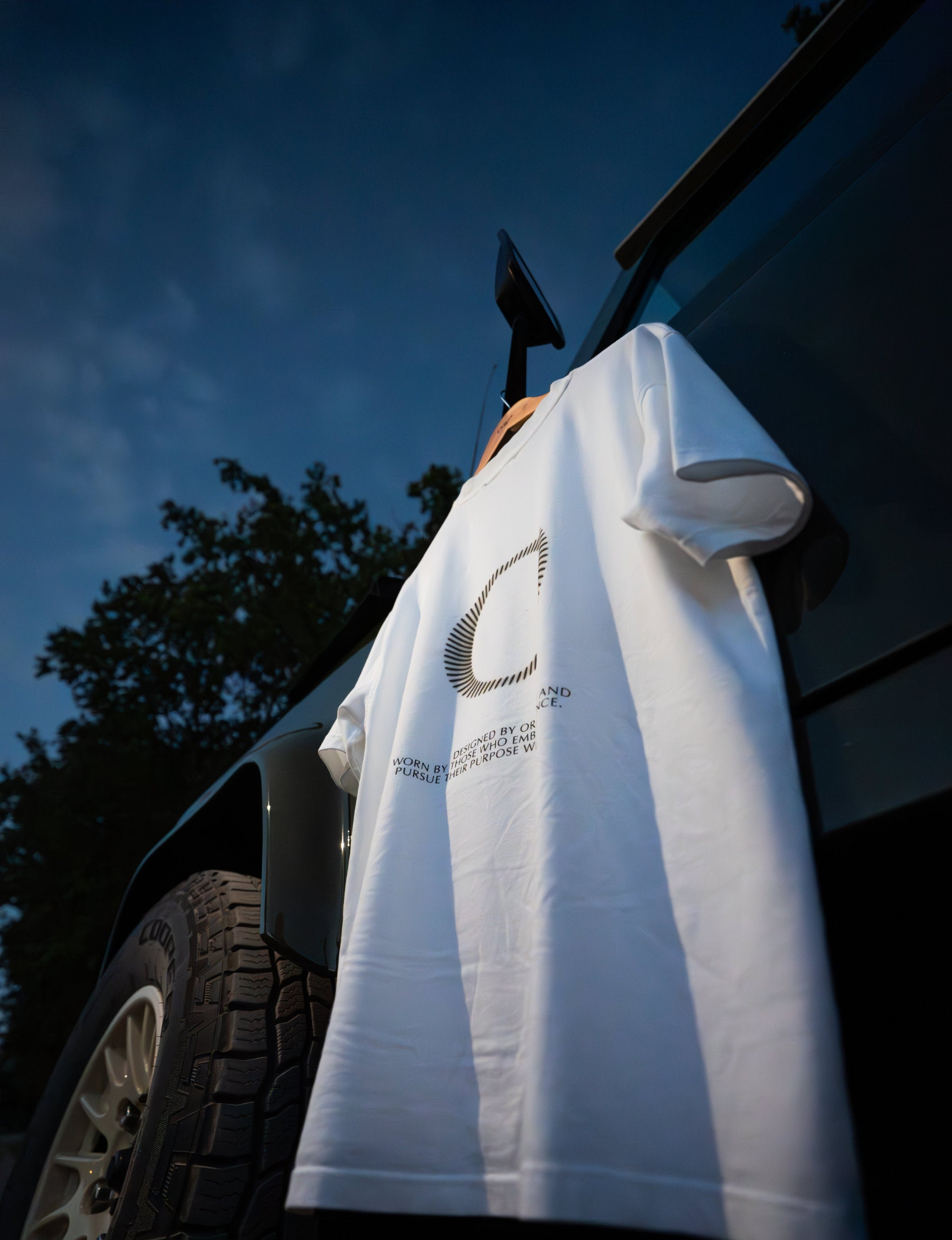 White Origin. Slash Tee hanging on a  Land Rover Defender door against a blue sky.